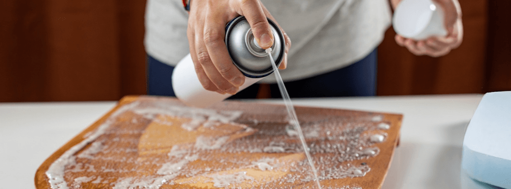 Guide on how to glue foam. Person spraying a contact spray adhesive onto wood to glue a foam seat pad to it
